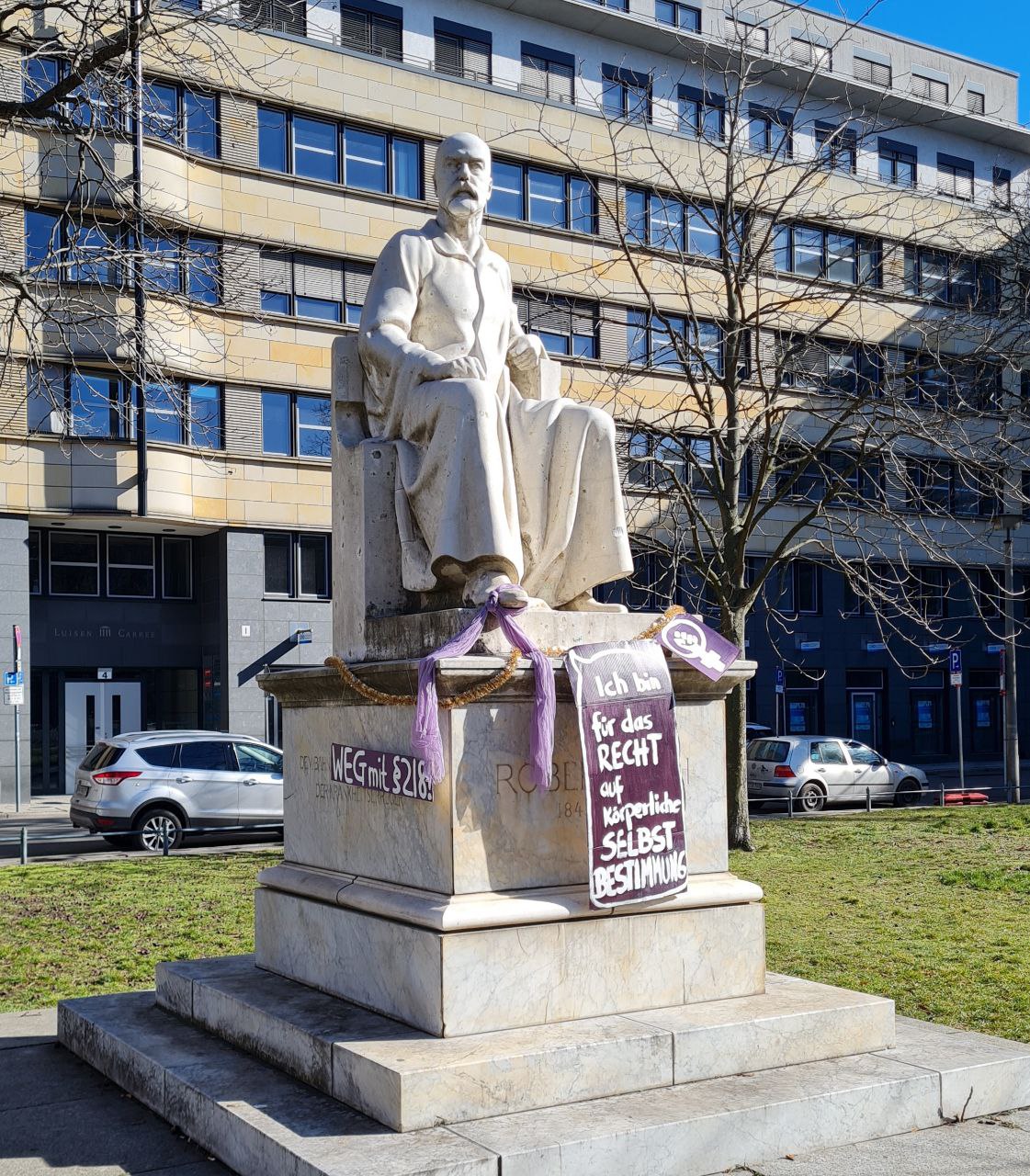 Das Foto zeigt eine Statue von Robert Koch am Campus Nord, die zum feministischen Kampftag (2021) von Demonstrant*innen verziert wurde.