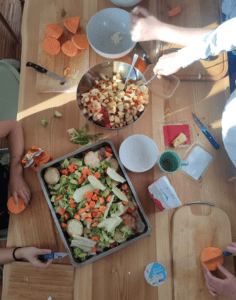 People prepare a vegetable dish together at a wooden table.